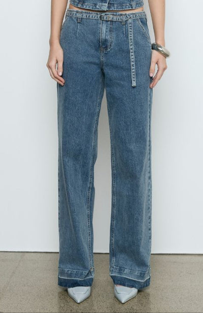Model wears the SOVERE Dawn Denim Pant in Vintage Blue. Full-length mid-rise jeans with belt and contrast hem detail.