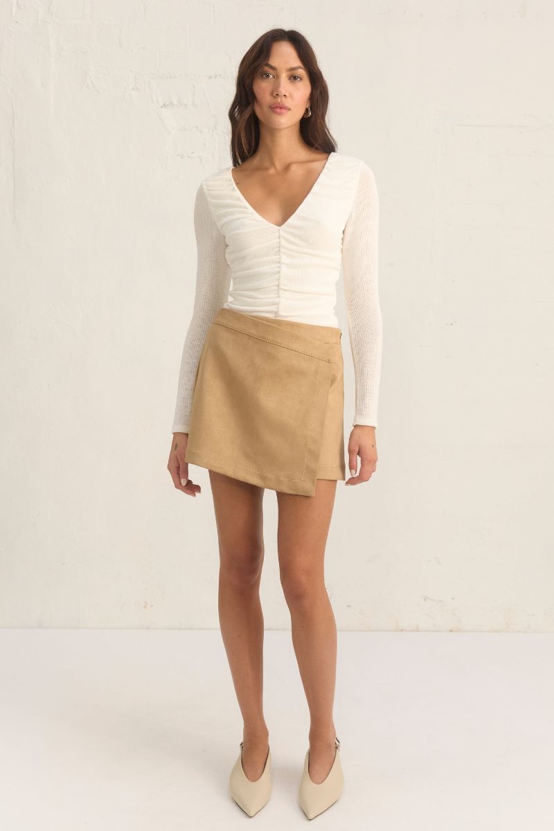 
Model wearing the Mon Renn Regenerated Top in cream — a deep V long-sleeve knit top with ruched sides and a body-skimming fit.
