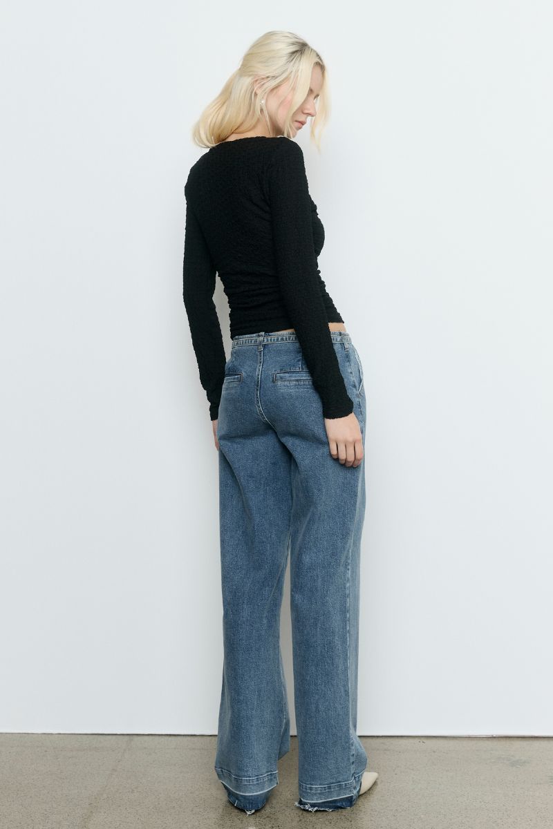 Model wearing the SOVERE Studio Solstice Top in black — a fitted, long-sleeve stretch top with an asymmetrical neckline.