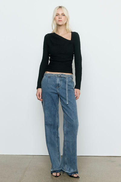 Model wearing the SOVERE Studio Solstice Top in black — a fitted, long-sleeve stretch top with an asymmetrical neckline.