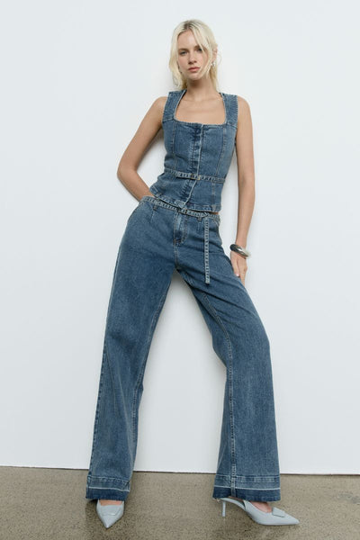 Model wears the SOVERE Dawn Denim Pant in Vintage Blue. Full-length mid-rise jeans with belt and contrast hem detail.