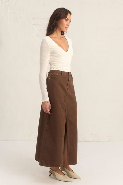 Model wearing the Mon Renn Bayside Denim Skirt in coffee — a high-waisted A-line brown denim midi skirt with a front split.
