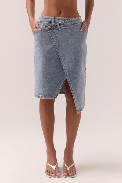 Model wearing the SOVERE Studio Etch Denim Wrap Skirt in light blue, featuring asymmetrical hem and double button waist.