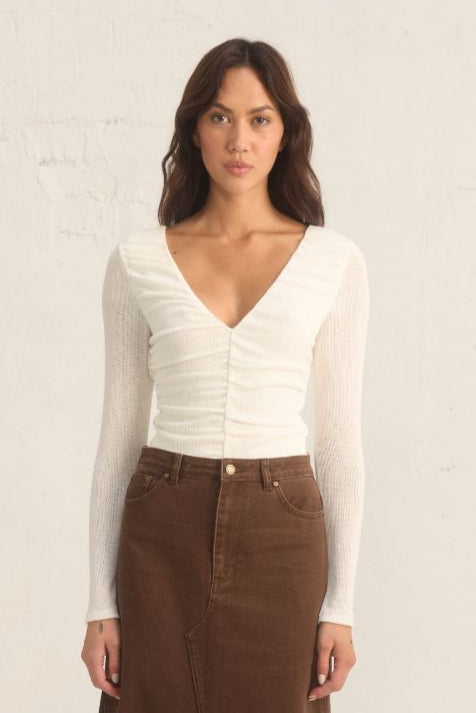 
Model wearing the Mon Renn Regenerated Top in cream — a deep V long-sleeve knit top with ruched sides and a body-skimming fit.
