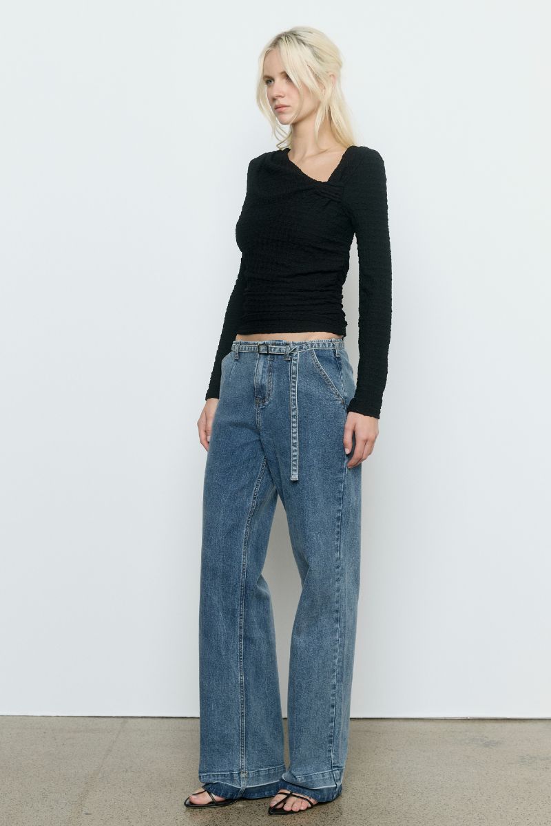 Model wearing the SOVERE Studio Solstice Top in black — a fitted, long-sleeve stretch top with an asymmetrical neckline.