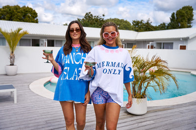 Oversized Hibiscus Hotel Mermaids Only Lounge Tee in white with bold blue graphics, styled for poolside.